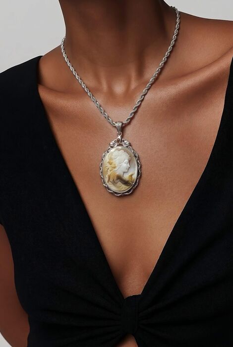 A silver-toned rope chain necklace featuring an oval-shaped cameo pendant. The pendant displays a carved profile of a figure in cream and brown tones, set within an ornate, texture