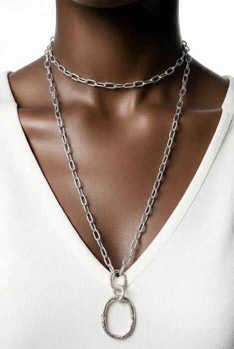 A silver-toned necklace featuring a double-layered chain design. The shorter chain sits as a choker, while the longer chain extends downward, ending in two interlocking circular pe
