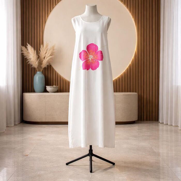 White sleeveless dress featuring a large pink flower design on the front. The dress is displayed on a black mannequin stand. The background includes a wooden wall, a beige cabinet,